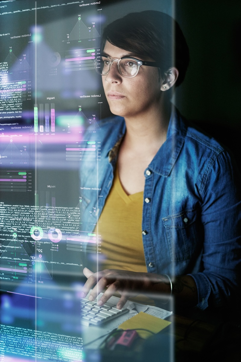 A focused individual working on a computer, with transparent screens displaying various data visualizations, graphs, and code. The image represents Ascend's expertise in software testing, data testing, IT staffing, application management services, software development, and systems integration. It highlights the company's commitment to delivering precise and efficient IT solutions across different industries.